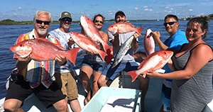 Six people on fishing charter holding 8 large fish.
